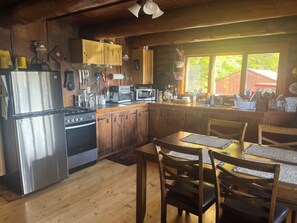 Eine Holzhütte mit Küche, inklusive Kühlschrank, Herd, Backofen und einem Essbereich mit Stühlen und Tisch.