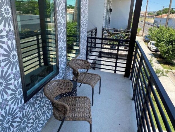 Relax on the balcony with two comfortable chairs, taking in the view of the surrounding street and lush greenery.