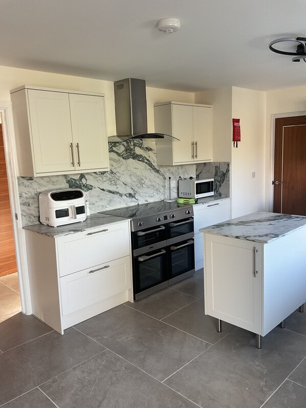 A kitchen with white cabinets, a stove, a microwave, and a marble backsplash. - Cosy Rural Bungalow In Cornwall between Falmouth and Helston Nr Penryn Campus (Nr Penryn Cornwall)