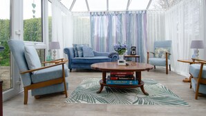 Un invernadero con un sofá azul, dos sillones, una mesita de centro con libros y una alfombra estampada.