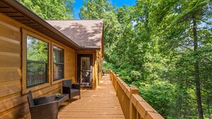 Une cabane en bois dotée d’une terrasse, de grandes fenêtres et offrant une vue sur une forêt.