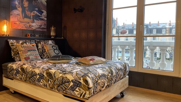 A bedroom with a large bed, a television on the wall, and a window with a view of buildings. - ★Studio Frères Lumière★Centre ville Dole - Wifi Netflix (Dole)