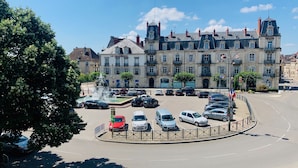A parking lot with cars, a fountain, and a historic building with multiple stories and balconies. - ★Studio Frères Lumière★Centre ville Dole - Wifi Netflix (Dole)