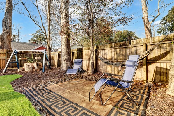 A backyard with a wooden fence, two lawn chairs, a hammock, and a swing set.