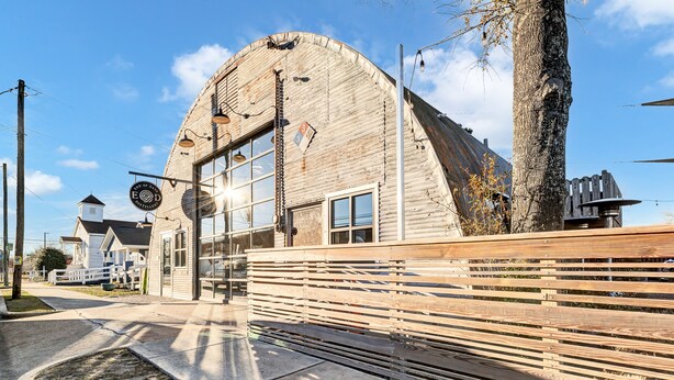 Ein rustikales Gebäude mit einer gebogenen Holzfassade, einem kleinen turmartigen Aufbau und einem Holzzaun.