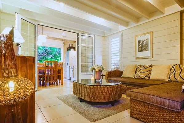 A modern living room with a glass coffee table, wicker sofa, and a dining area with wooden chairs.