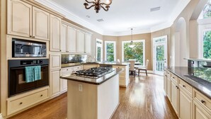 A spacious kitchen with a central island, built-in appliances, and large windows offering views of greenery.