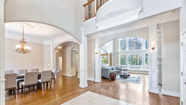 A spacious living room with a dining area, wooden flooring, and large windows offering a view of trees.