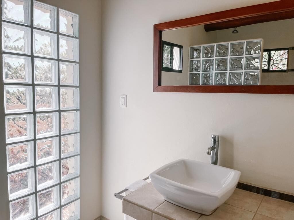 A bathroom with a large window, a white sink, and a mirror.