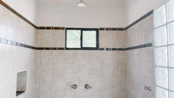 A shower area with tiled walls, a wooden beam ceiling, and a window.