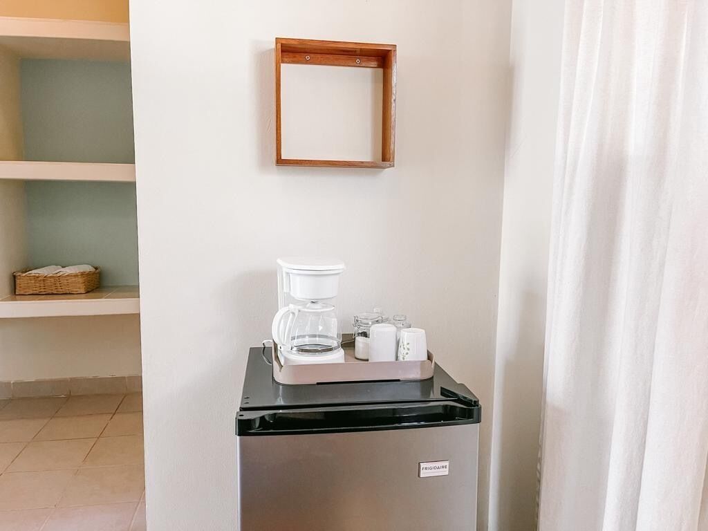 A kitchenette with a coffee maker, a small refrigerator, and a shelf with a basket.
