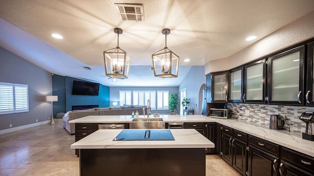 Una cocina moderna con armarios oscuros, una isla grande e iluminación colgante.