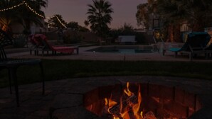 Un brasero al frente, con una piscina y sillones de descanso al fondo.