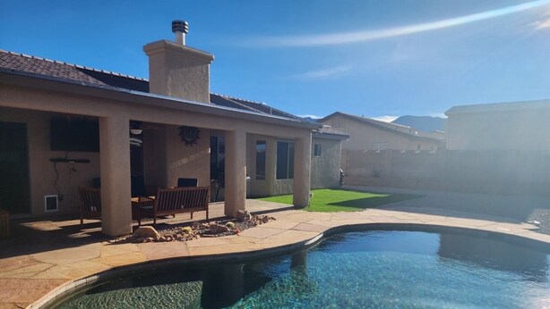 Una piscina cristalina con borde de piedra, un patio con banco y un edificio con chimenea.