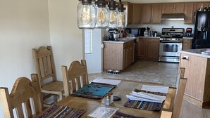Un comedor con una mesa y sillas de madera, una araña y una cocina al fondo.