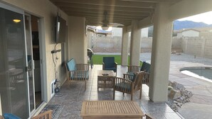 Un patio techado con mobiliario exterior, piscina y vistas a una cadena montañosa.
