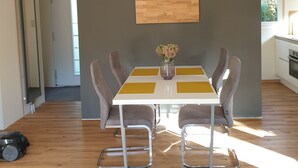A dining area with a white table, four chairs, and a wooden panel wall. - Vacation home "Ons Hüske" 50sqm in a quiet location  (Dirkshorn)