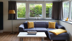 A modern living room with a grey sectional sofa, a white coffee table, and large windows with curtains. - Vacation home "Ons Hüske" 50sqm in a quiet location  (Dirkshorn)