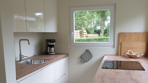 A modern kitchen with white cabinets, a stainless steel sink, a coffee maker, and a window with a view of greenery. - Vacation home "Ons Hüske" 50sqm in a quiet location  (Dirkshorn)