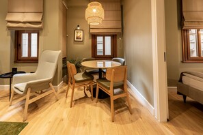 Un coin repas comprenant une table ronde et quatre chaises, un luminaire suspendu et deux fenêtres équipées de stores.