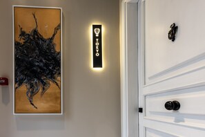 L’intérieur d’un hôtel, avec un tableau abstrait encadré, un panneau n éon indiquant « TOKYO » et une porte blanche dotée d’une poignée noire.