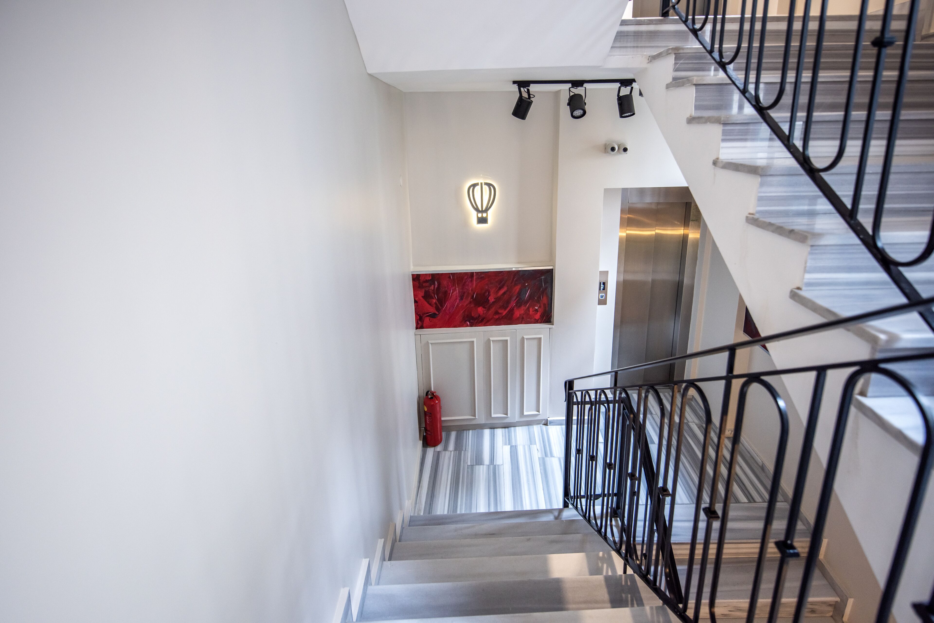 A modern staircase with a metal railing, a fire extinguisher, and a wall-mounted light fixture.
