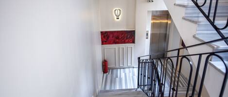A modern staircase with a metal railing, a fire extinguisher, and a wall-mounted light fixture.