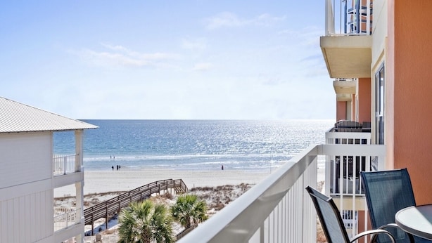 A balcony with a view of the beach, a pool area, and a dining table. - Beachfront - 2 Kings - Heated Pool - Hot tub - Low Density (Orange Beach)