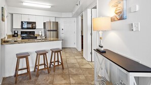 A modern kitchen with white cabinetry, stainless steel appliances, a granite countertop, and three wooden stools. - Beachfront - 2 Kings - Heated Pool - Hot tub - Low Density (Orange Beach)