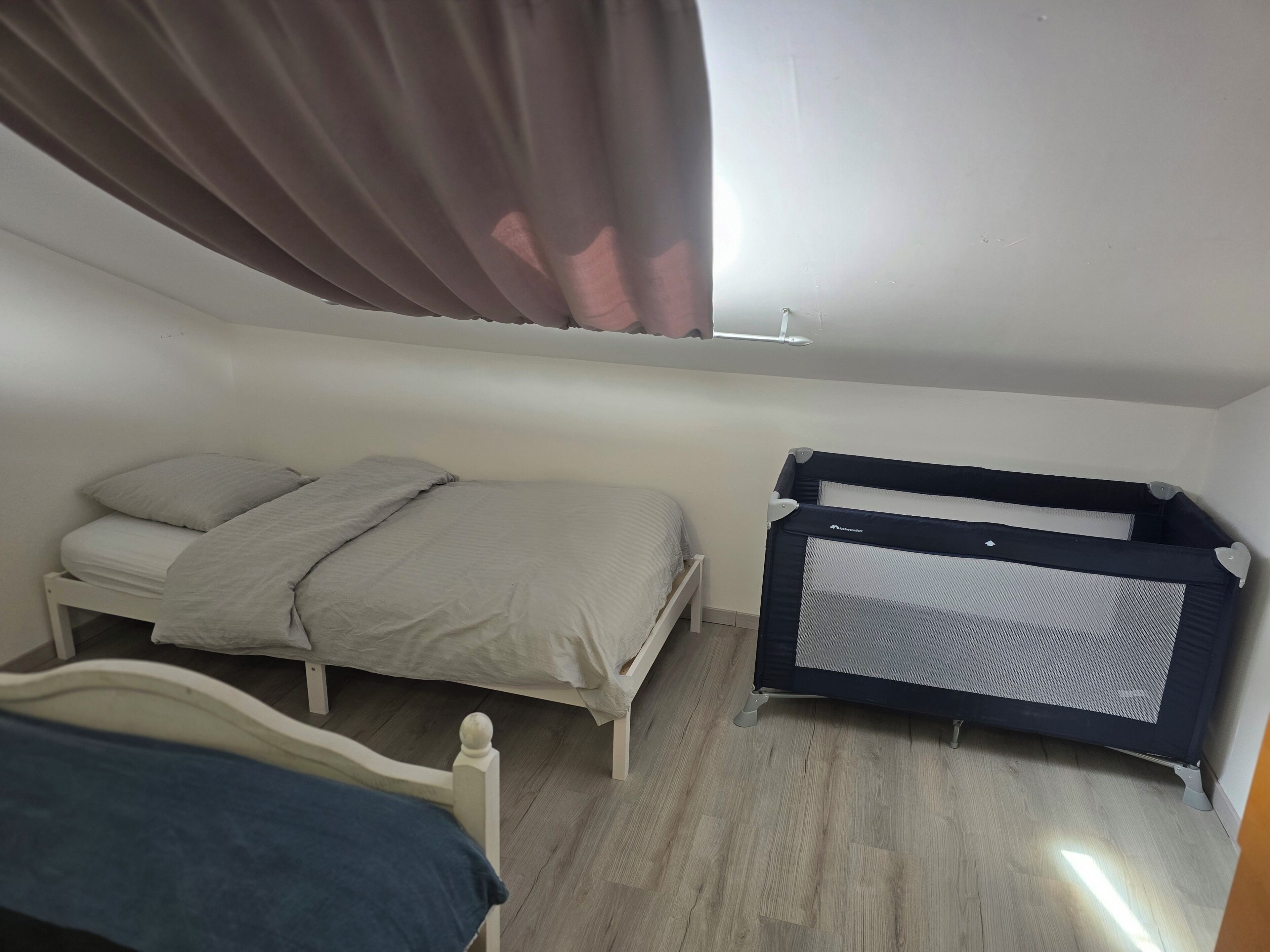 Une chambre à coucher avec un lit, un berceau et une fenêtre avec des rideaux.