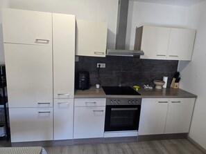 A modern kitchen with white cabinets, a built-in oven, a coffee maker, and a stove.