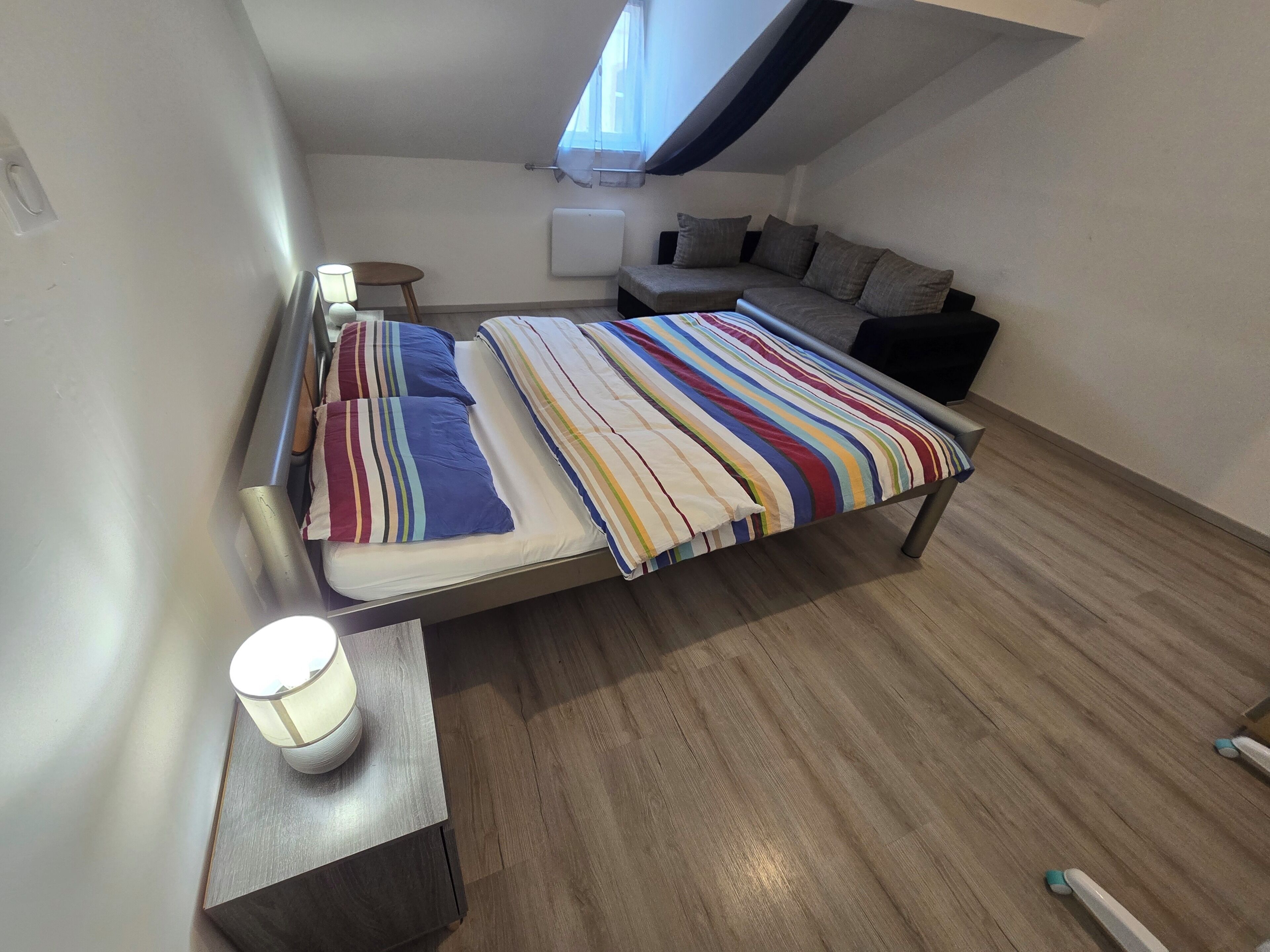 Una camera da letto con un letto, un comodino con una lampada, una finestra e un termosifone.