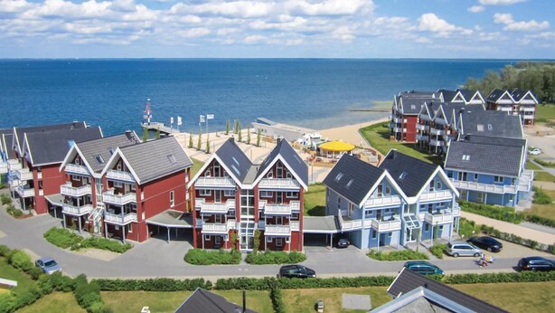 Een kustgebied met woonhuizen, een strand en een vuurtoren in de verte.