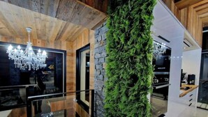 Ein modernes Interieur mit Holzbalkendecke, einer Kandelaberleuchtreihe, einer Steinsäule mit Pflanzen und einer Küchenzeile.