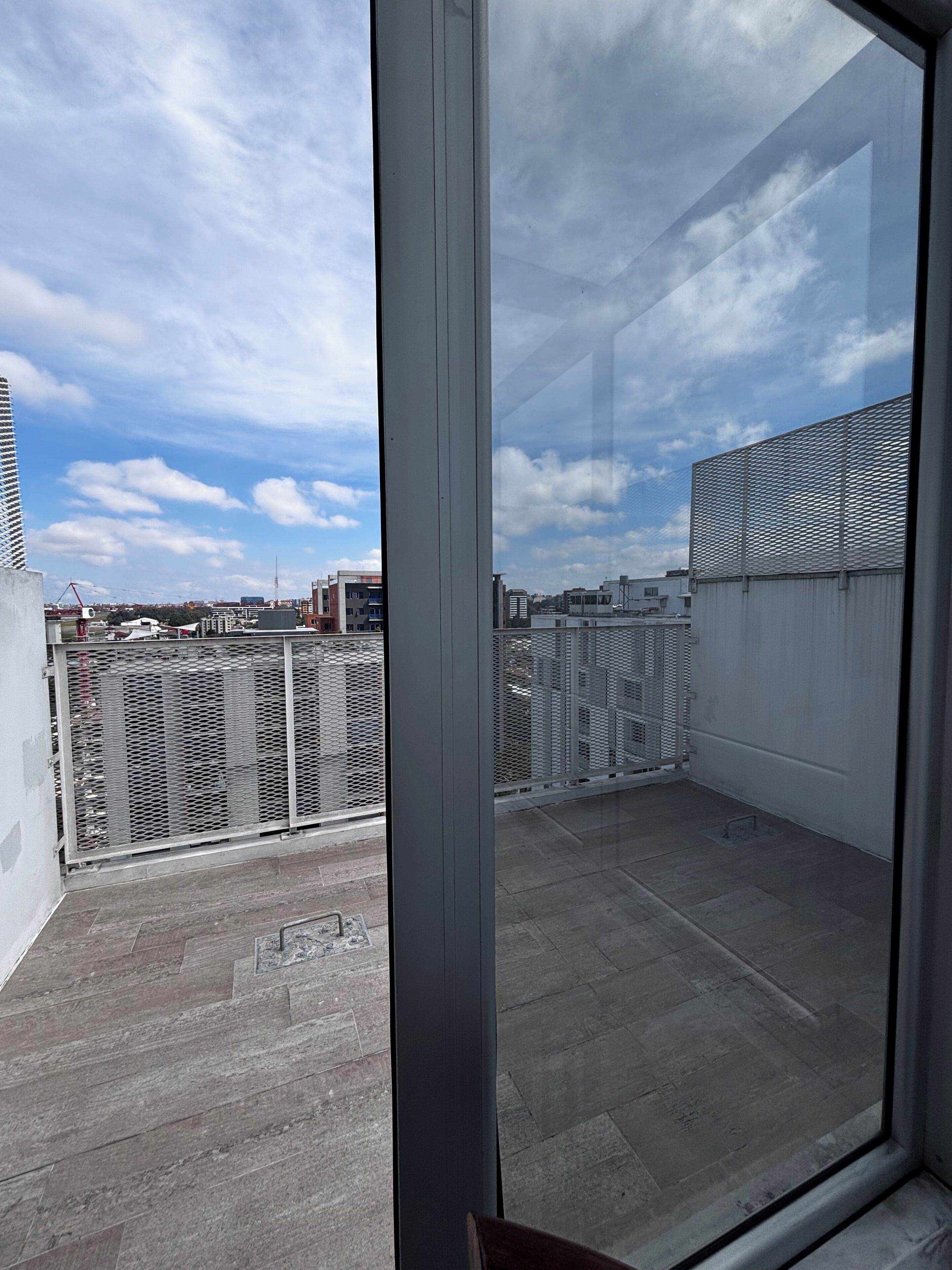 Un balcon avec une balustrade en métal, une vue sur le paysage urbain et un ciel dégagé.