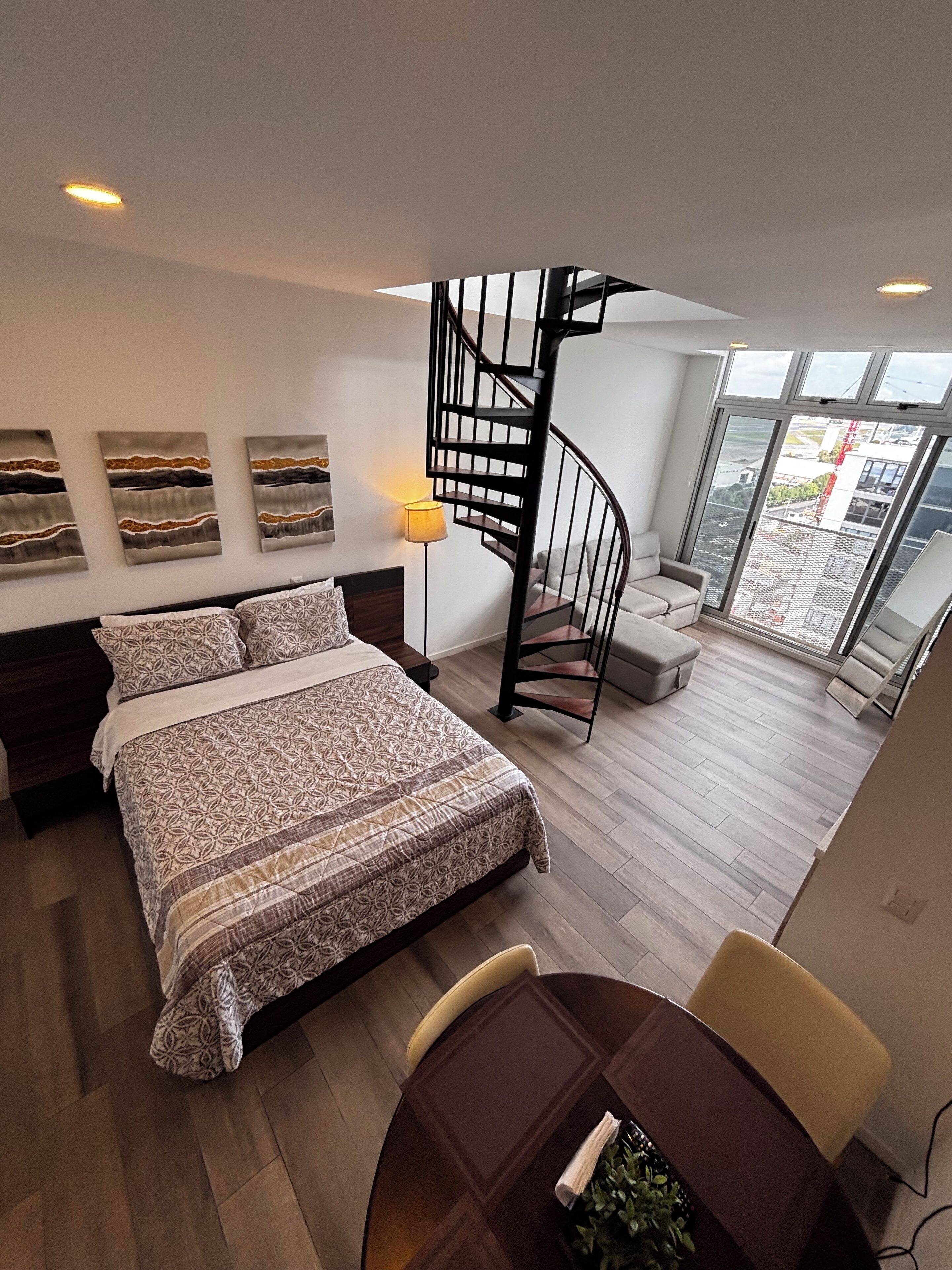A modern bedroom with a large bed, a spiral staircase, and a balcony with a view.