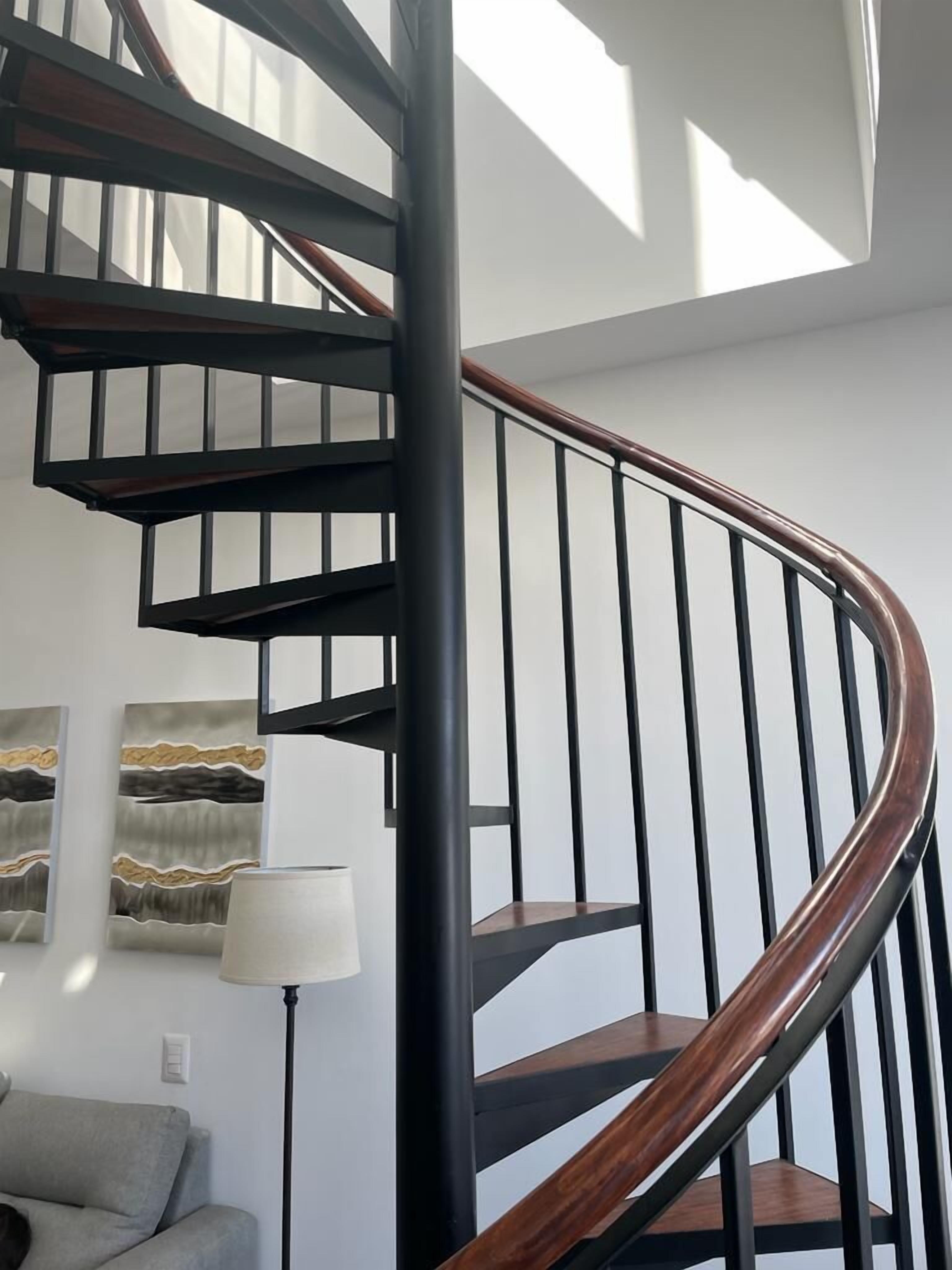 A modern spiral staircase with black metal railings and wooden steps.