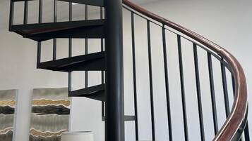 A modern spiral staircase with black metal railings and wooden steps.