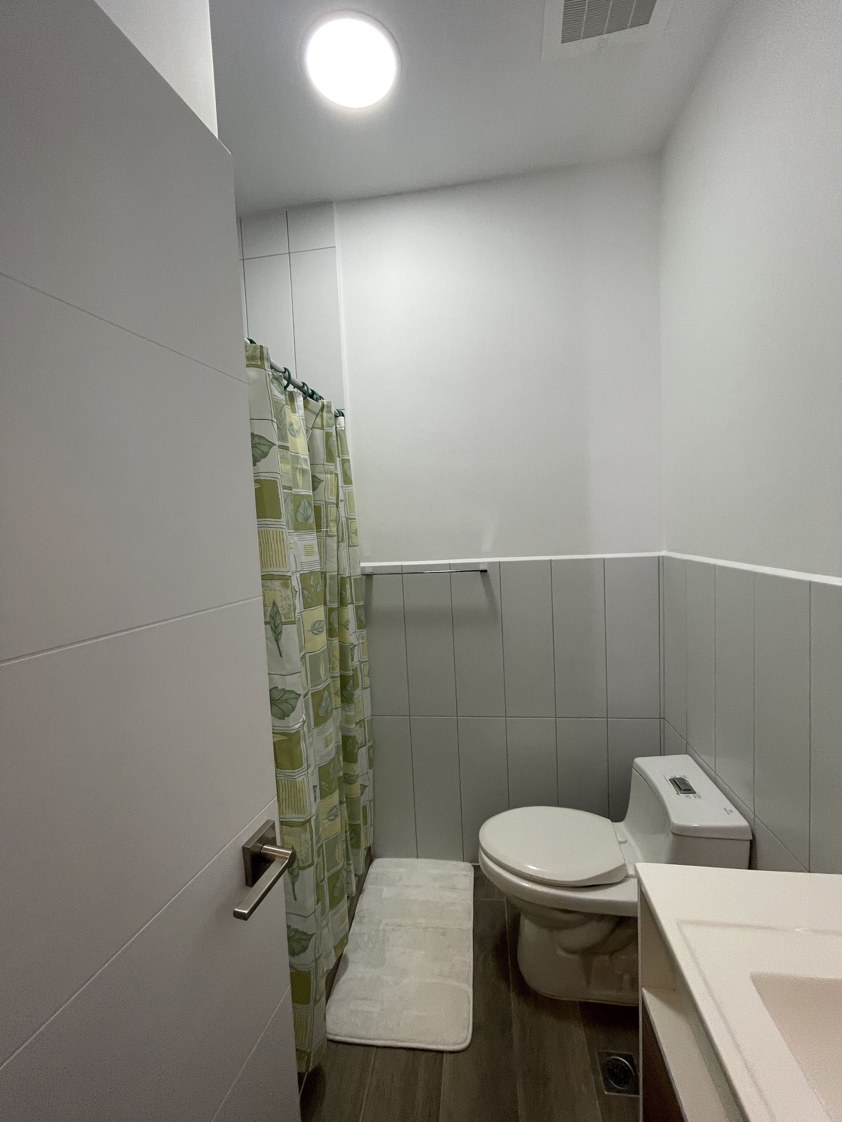 A small, modern bathroom with a toilet, a shower curtain, and a white sink.