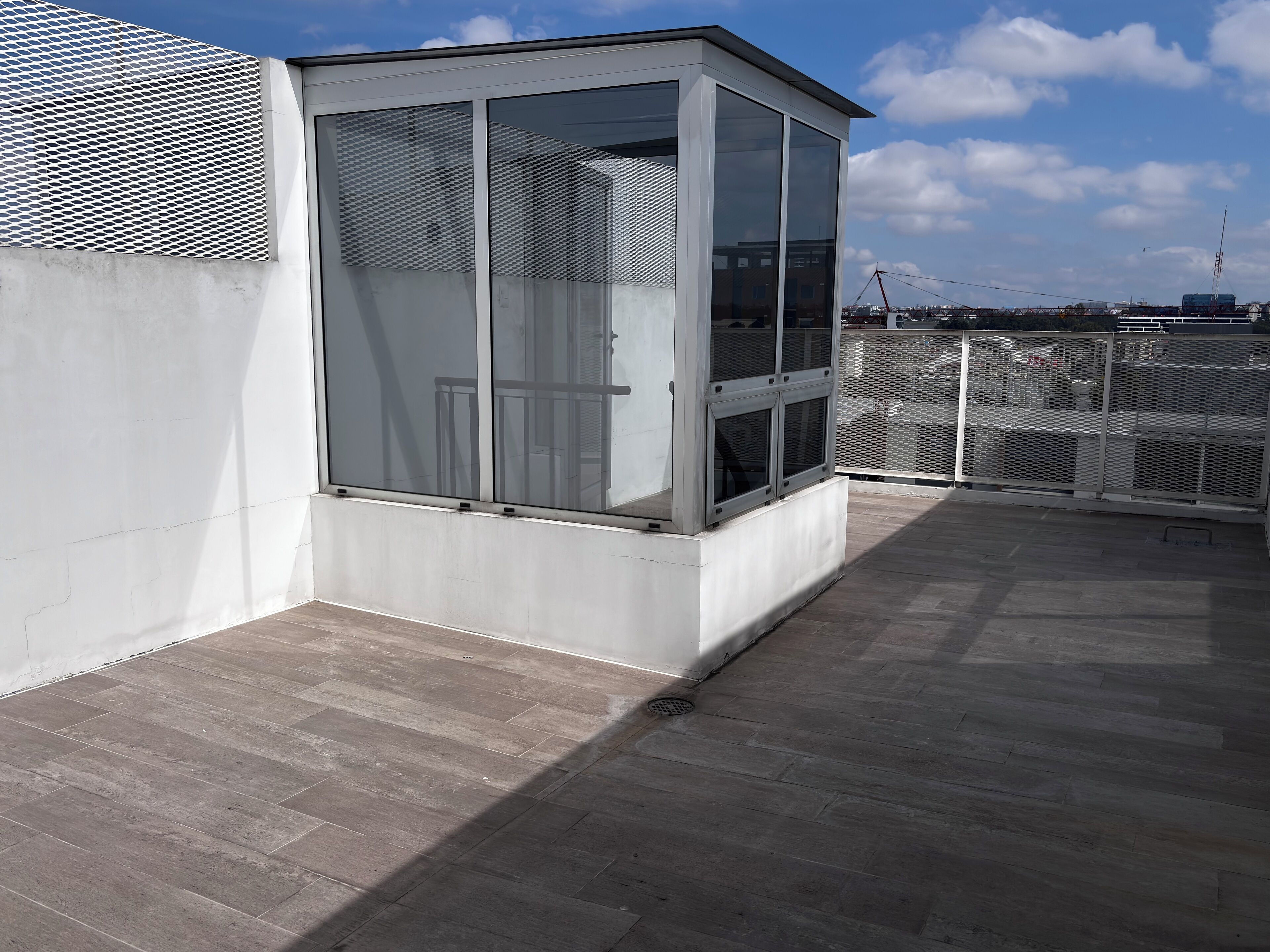En moderne bygning med stor glasfacade, hegn af metalnet og et tag med tagsten.