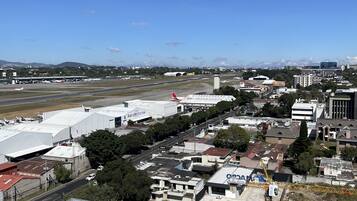 Vista aérea de un aeropuerto con varias edificaciones, incluyendo un hangar blanco grande y un edificio blanco más pequeño con la leyenda “AeroMotors”. Se observan varios vehículos en el suelo, y una grúa de construcción es visible en primer plano.