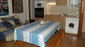 Una cuina compacta amb armaris de fusta, microones, rentadora i zona de dinar amb taula i tamboret.