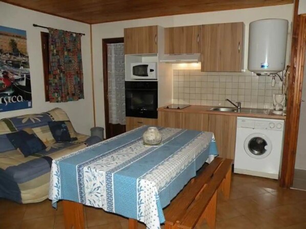 Cocina compacta con armarios de madera, microondas, lavadora y comedor con mesa y banco.