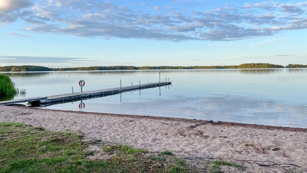 Un lago tranquilo con una playa de arena y un muelle de madera que se adentra en el agua.
