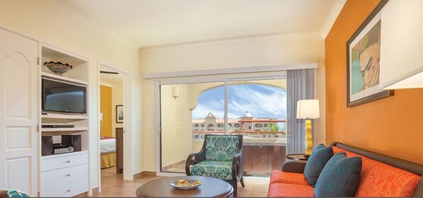 A hotel room with a television, a sofa, a chair, and a balcony with a view of buildings.