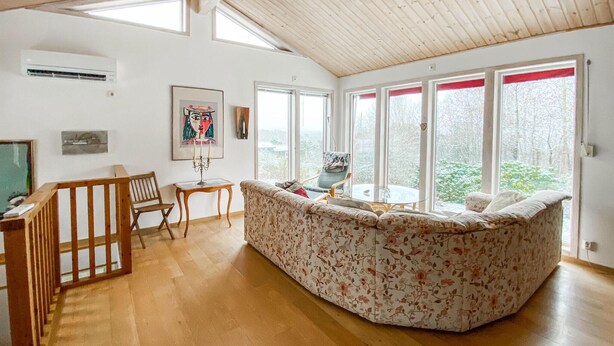 A cozy living room with a wooden ceiling, large windows, a floral sofa, a wooden chair, and a small table. - Beautiful home in Falkenberg with WiFi (Falkenberg)