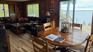 L’intérieur chaleureux d’un chalet avec un plancher en bois, un canapé en cuir, une table à manger avec des chaises et une grande fenêtre donnant sur un lac.