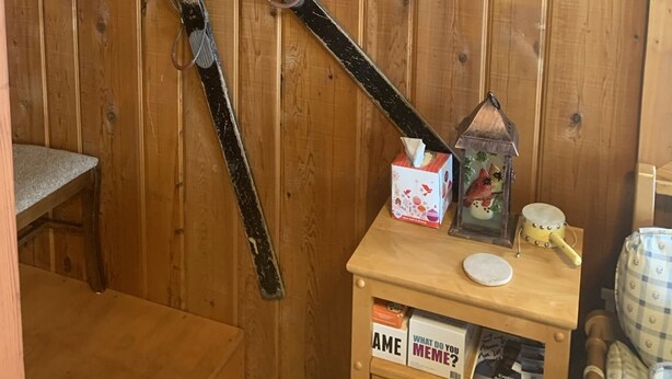 Un mur en bois, avec une grande paire de skis d’aspect rustique appuyée contre lui, une pancarte indiquant « Bienvenue à Big Bay » et une petite étagère en bois sur laquelle sont disposés divers objets.