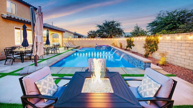 Un patio trasero con piscina, mobiliario exterior y una chimenea.