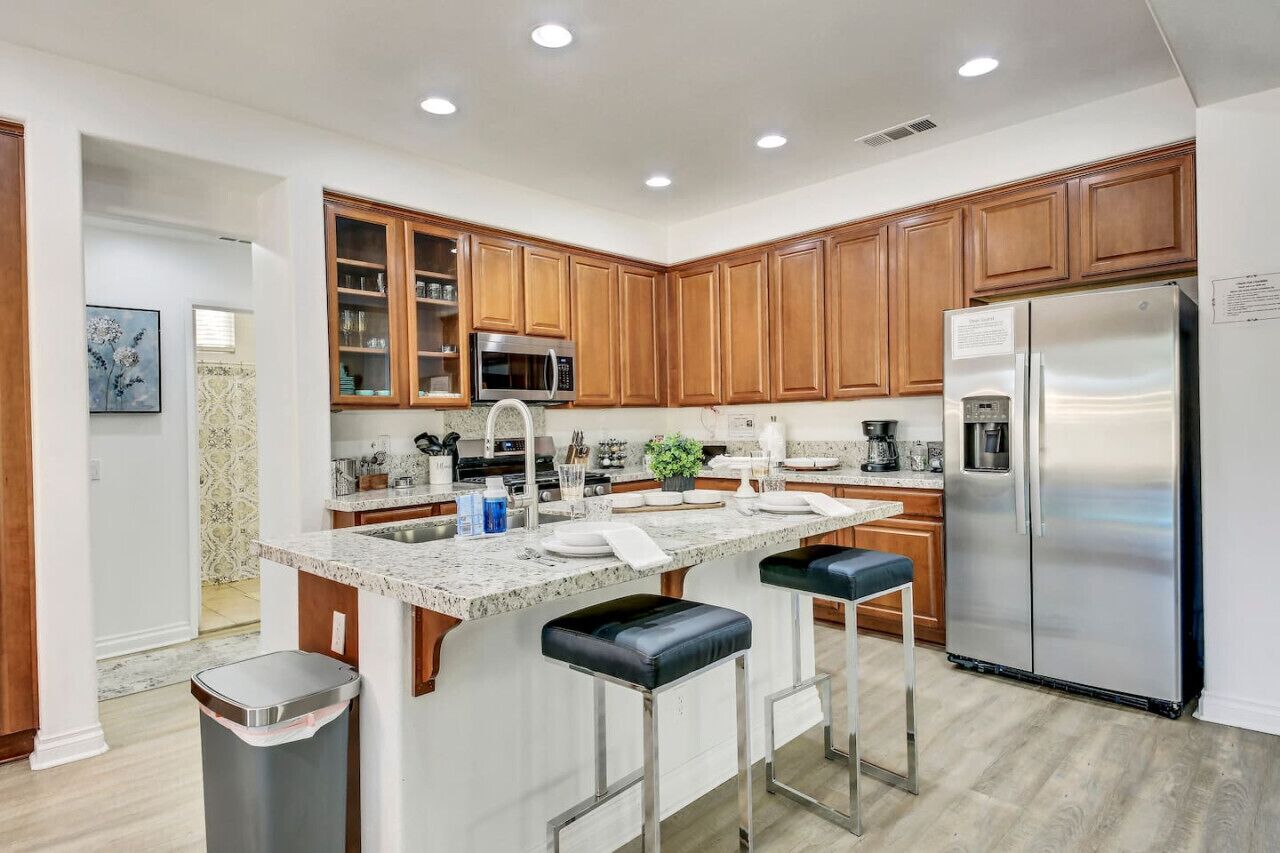 A modern kitchen with wooden cabinets, stainless steel appliances, a granite countertop, and a central island with bar stools.